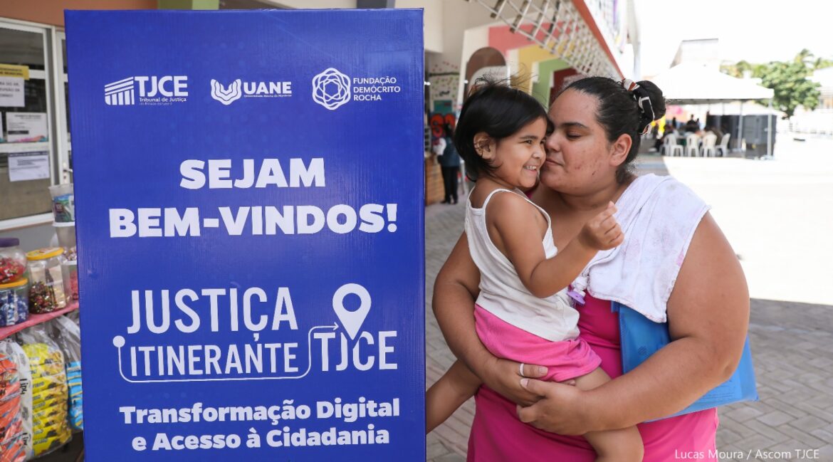 Mulher com a filha no braço e, ao lado dela, um banner do Justiça Itinerante
