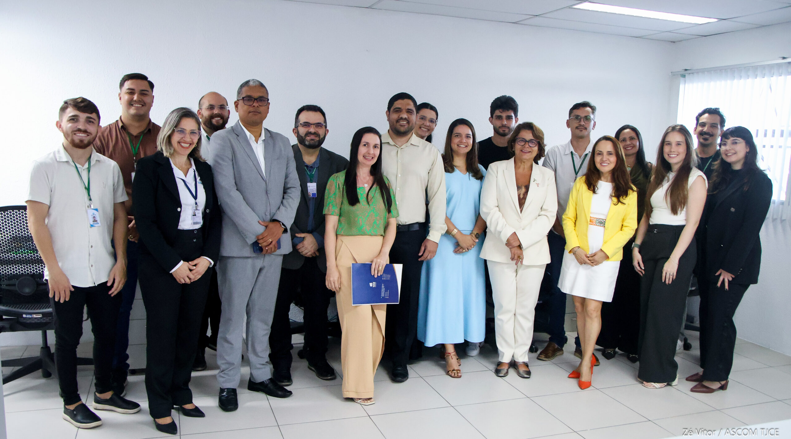 Imagem mostra várias mulheres e homens posando para foto, sorrindo em pé, em uma sala