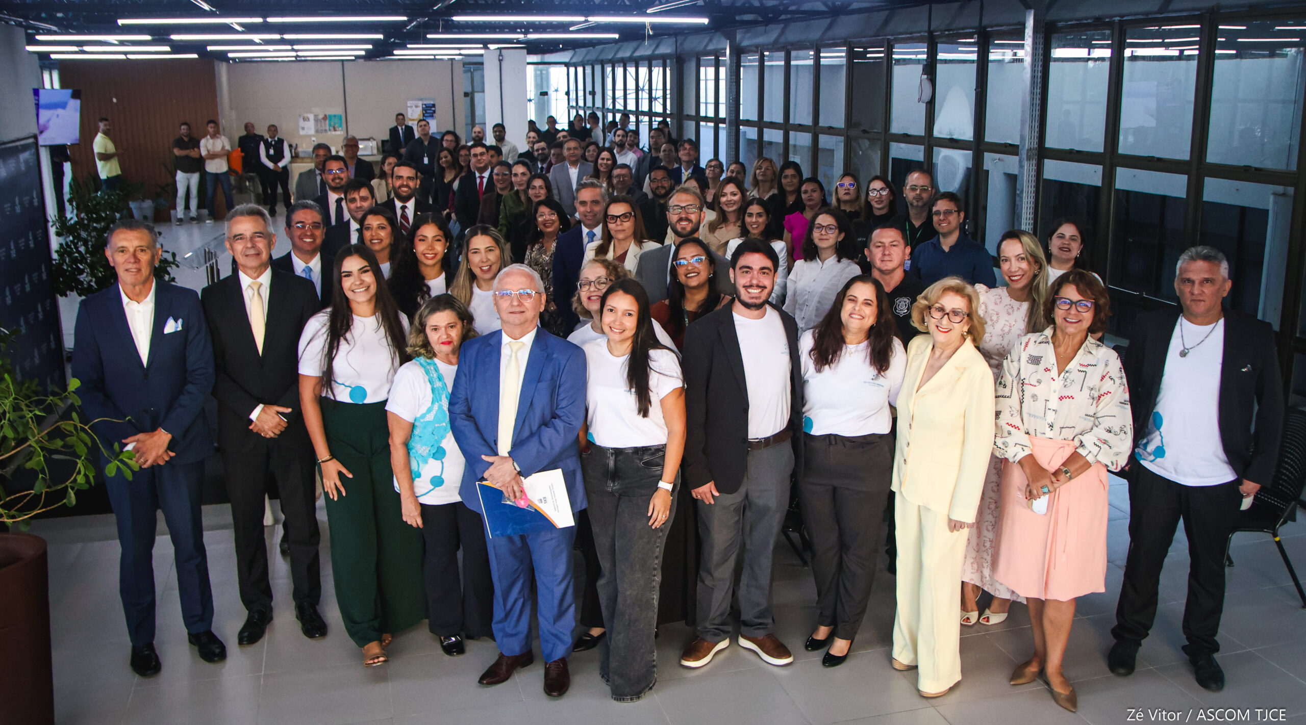 Foto de várias pessoas em pé, posando para foto, ao final do evento, sorrindo, em um grande salão
