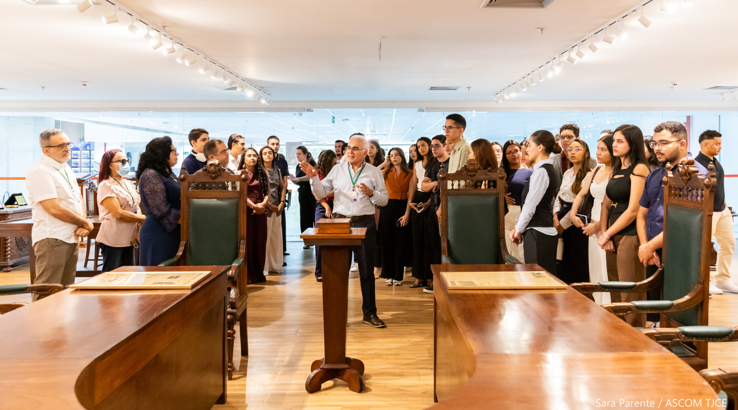 Várias mulheres e homens conhecendo o espaço do Memorial. Ao centro, um homem dando as explicações sobre as relíquias expostas no local