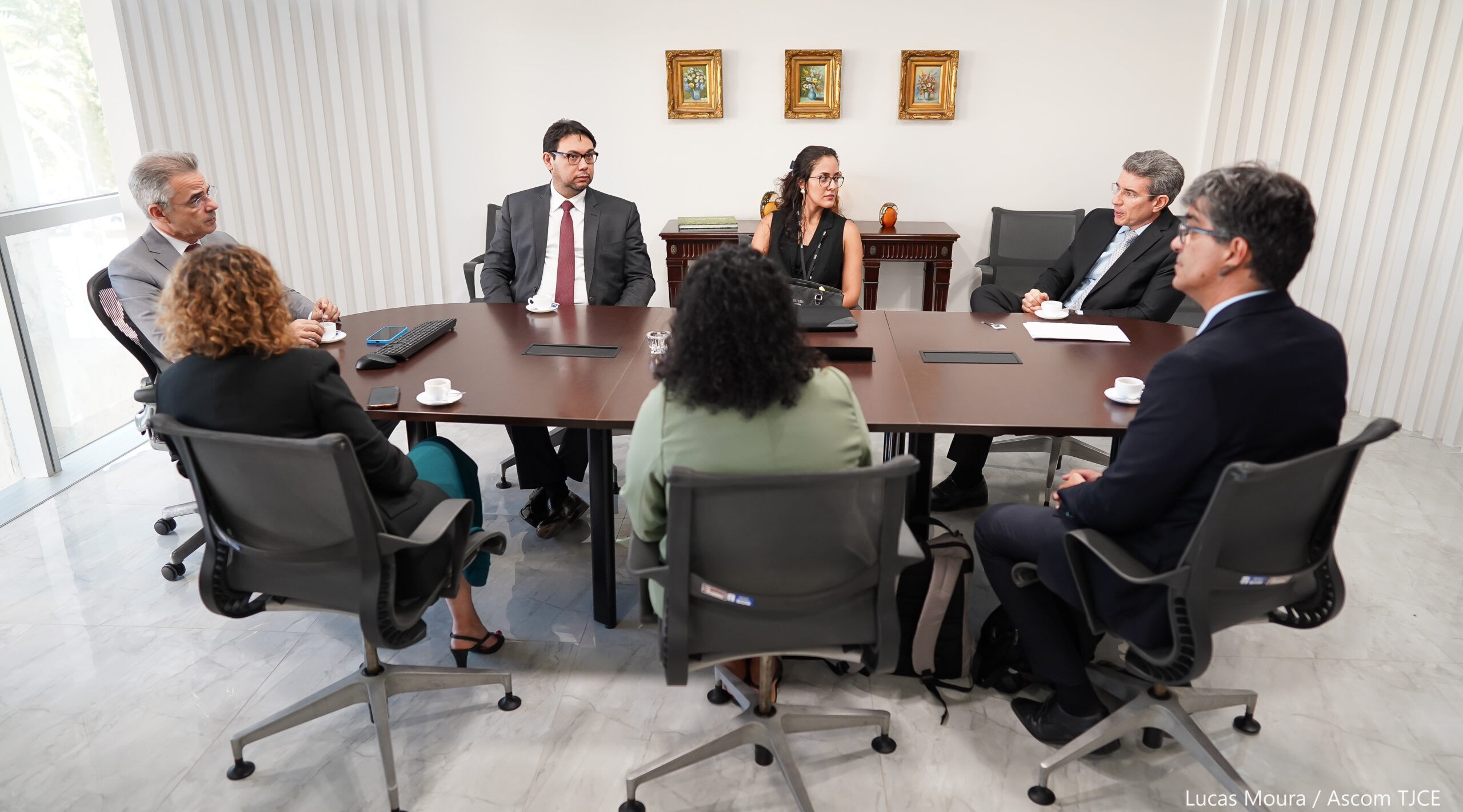 Imagem de várias pessoas sentadas ao redor da mesa, dialogando em uma sala