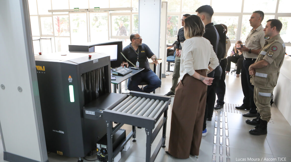 A imagem mostra pessoas observando a instalação de equipamento de segurança, na verdade, um equipamento de raio-X,na entrada principal do prédio do tribunal