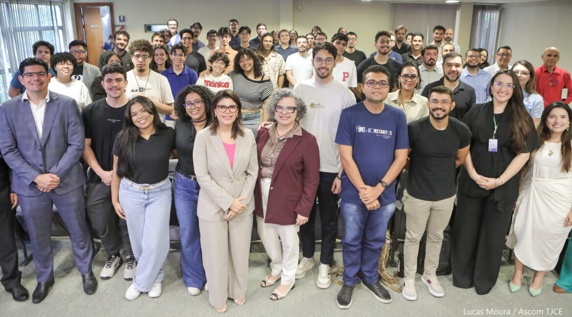 Imagem de várias mulheres e homens sorrindo para foto, em pé, num grande auditório