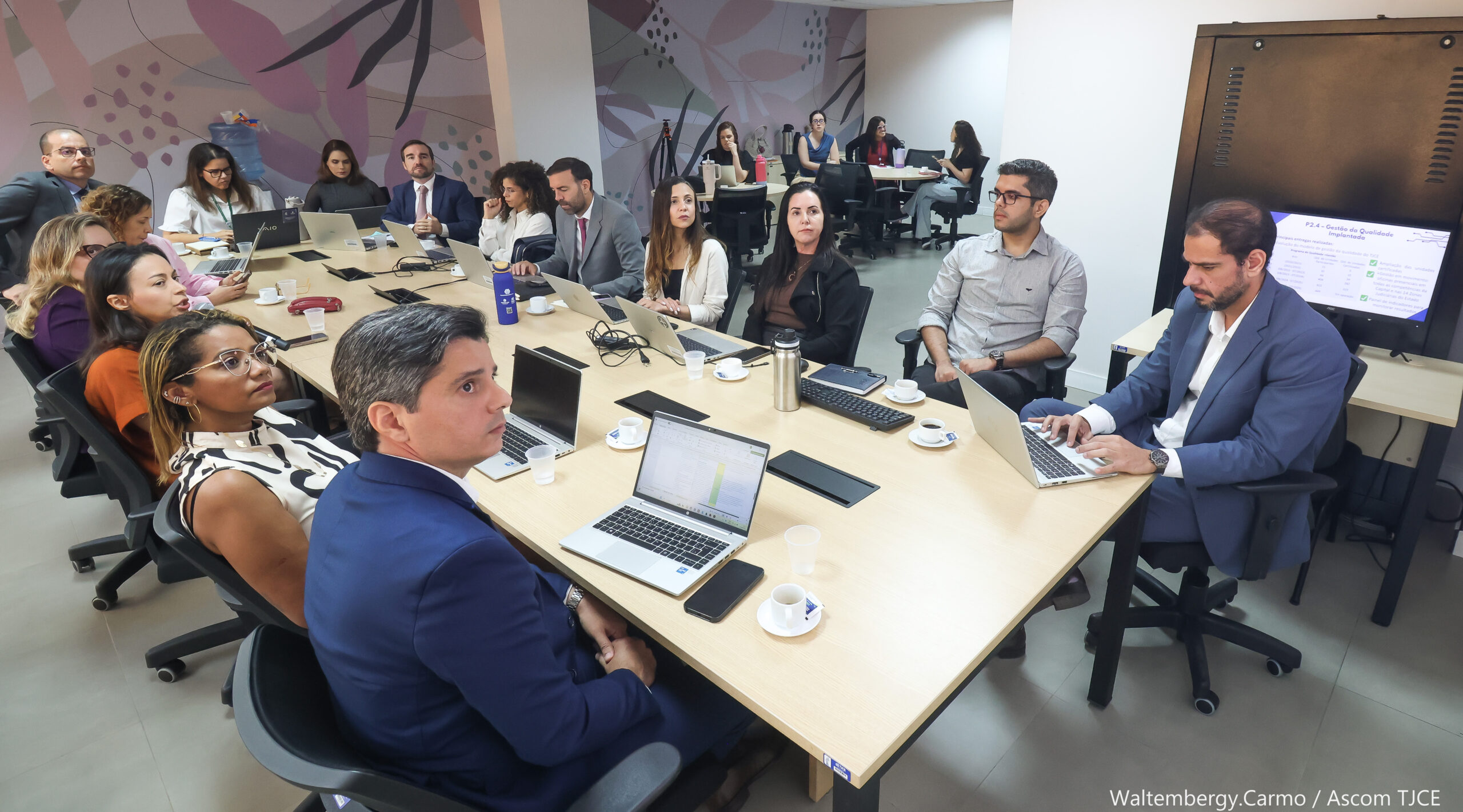 Imagem mostra várias mulheres e homens sentadas ao redor de uma grande mesa de trabalho, dialogando em uma sala