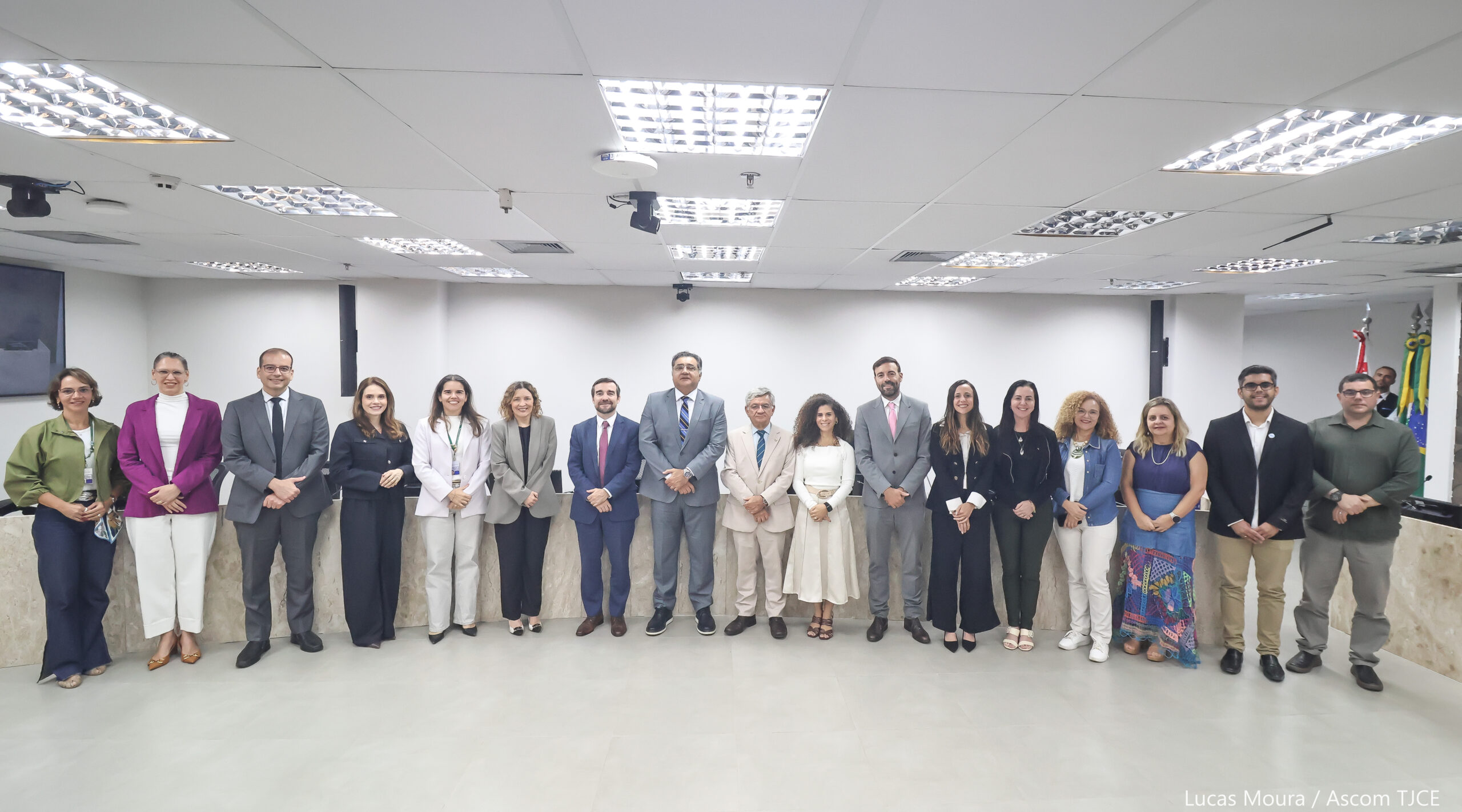 Imagem mostra vários homens e mulheres posando para foto, sorrindo, em pé, num grande auditório
