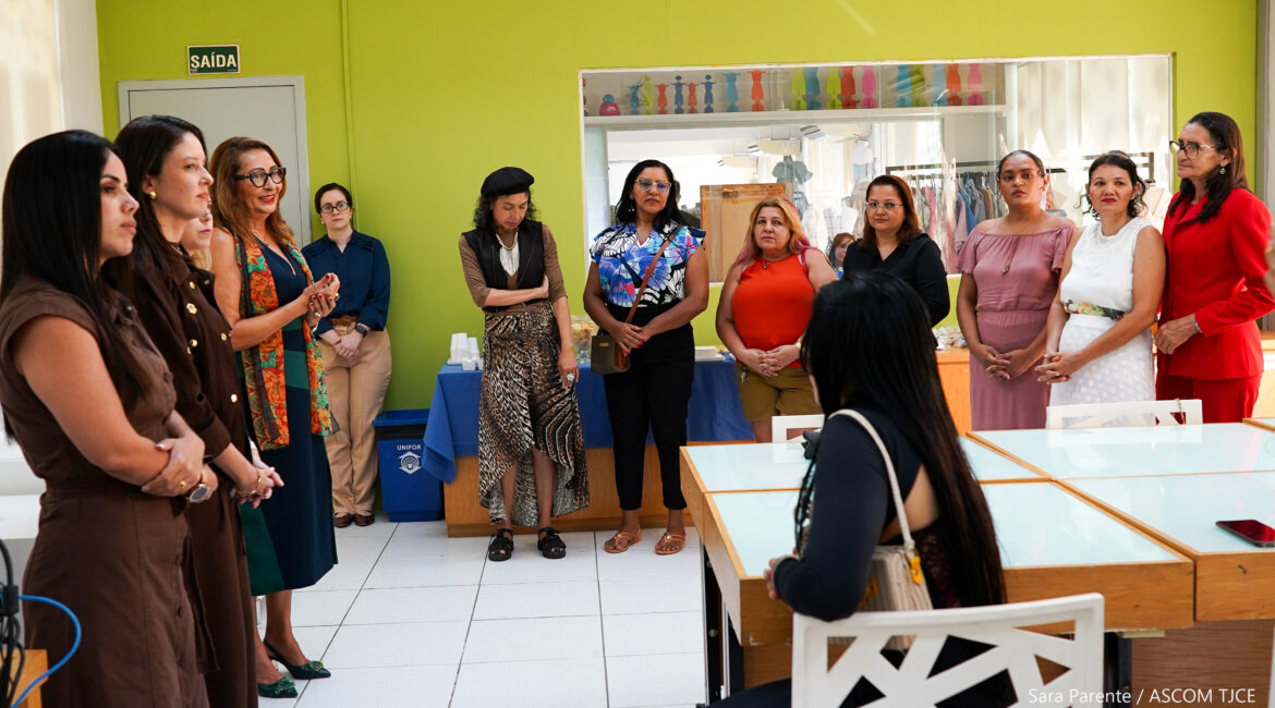 A imagem mostra várias mulheres em uma sala ampla, olhando umas para outras, muitas delas sorrindo