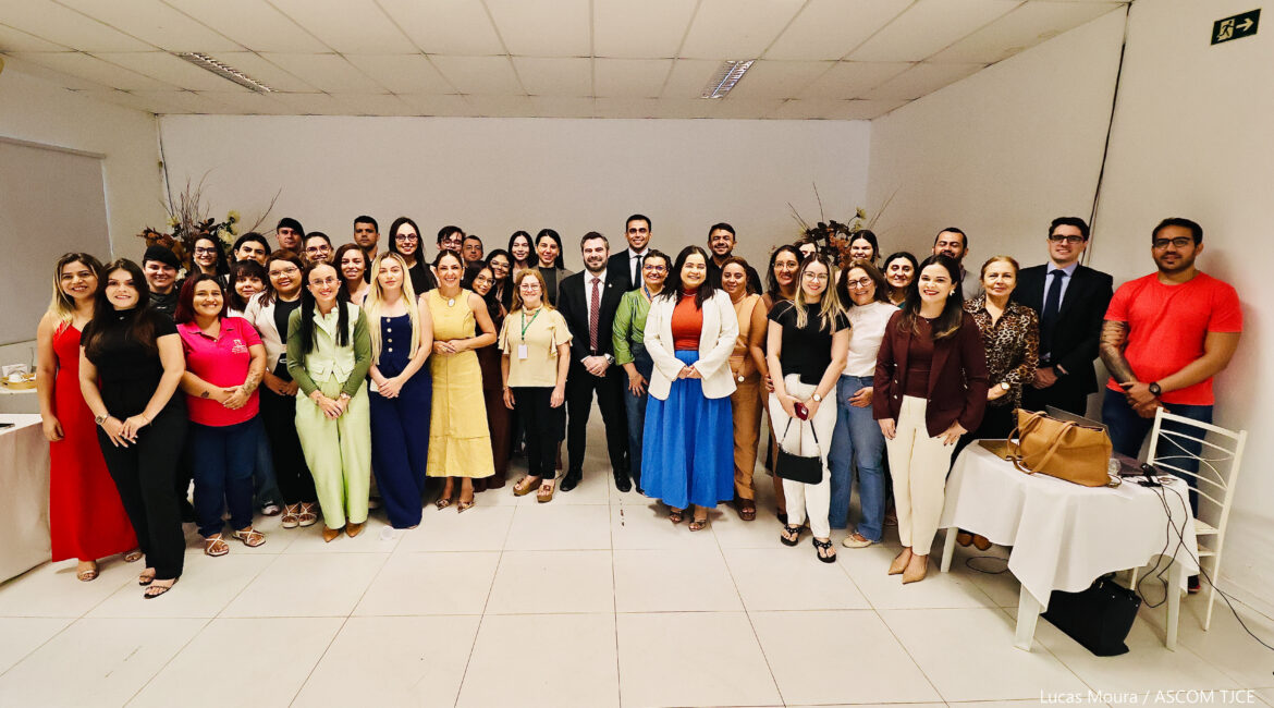 Várias mulheres e homens posando para foto, sorrindo, em pé, em um salão