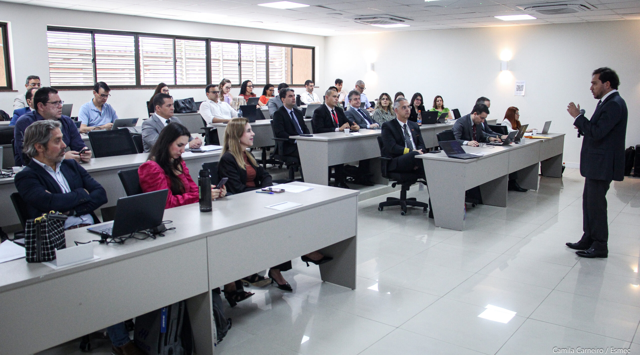 Homem falando ao microfone e, à frente dele, várias pessoas sentadas em um grande auditório, ouvindo suas explanações
