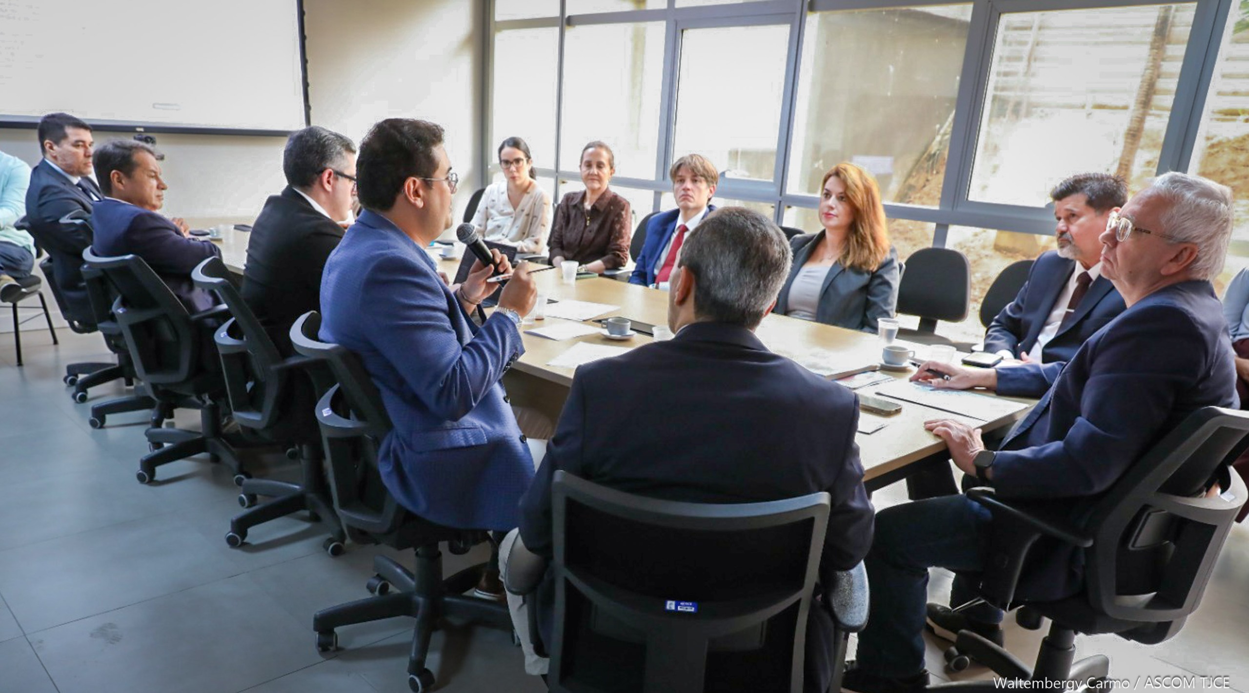 Foto de várias pessoas sentadas ao redor de uma mesa, dialogando, em uma sala
