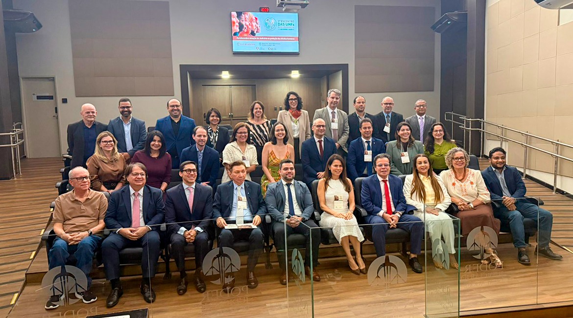 Imagem de vários homens e mulheres posando para foto, em pé e sentados, num auditório