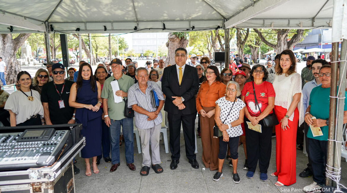 Várias mulheres e homens posam para foto, ao final do evento. Todas(os) estão sorrindo, em pé, pergilhadas(os) ao ar livre, debaixo de uma tenda